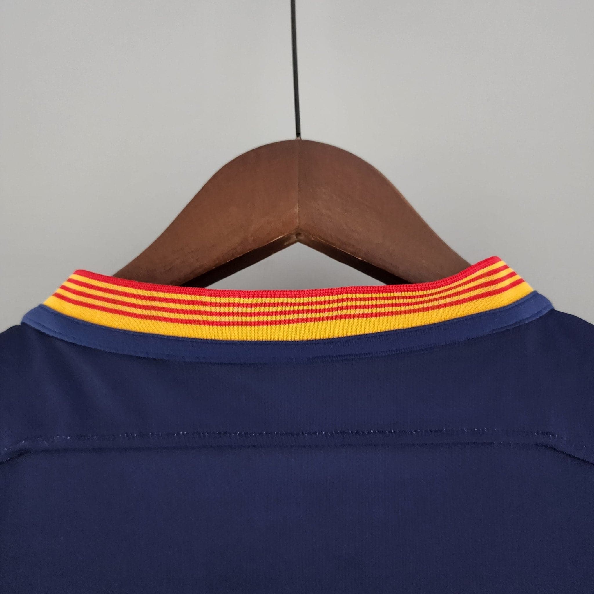 barcelona-classic-201516-final-with-messi-10-badges-jersey-521750 | AE JERSEY Blue garment on a wooden hanger with a bright red-yellow striped collar visible at the top edge.