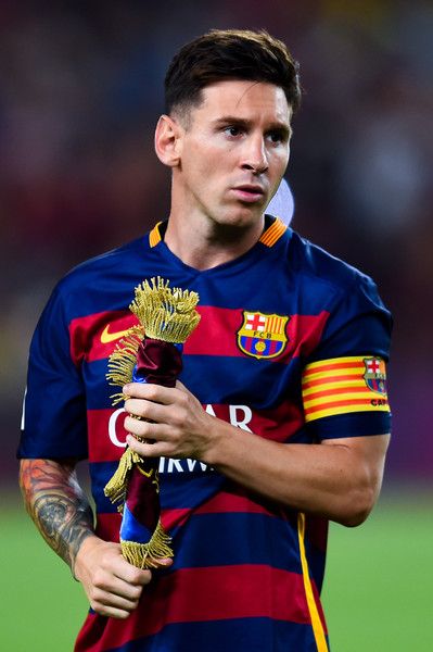 barcelona-classic-201516-final-with-messi-10-badges-jersey-720822 | AE JERSEY Soccer player in Barcelona jersey holding a ceremonial trophy with tassels on the field, wearing a captain's armband