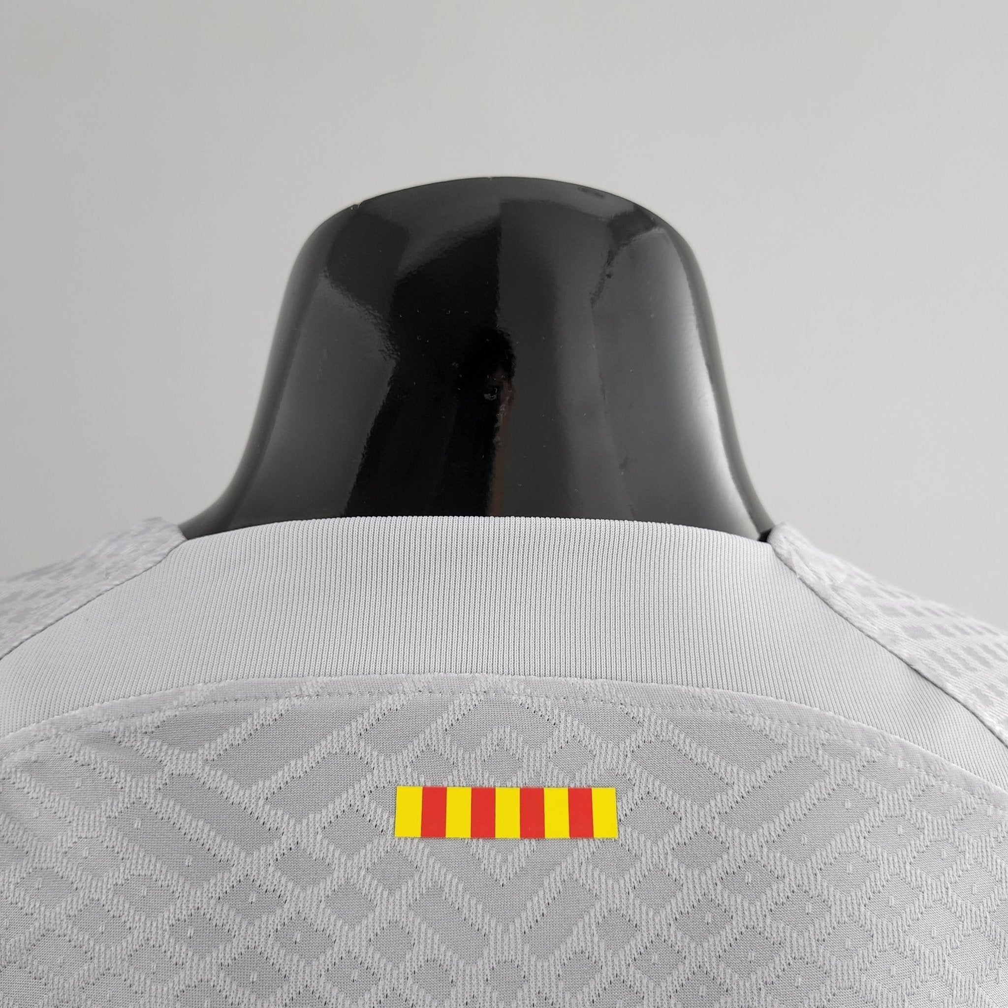 barcelona-third-player-version-jersey-202223-131970 | AE JERSEY Close-up of a shiny black curved surface against a light gray background, with a small yellow-and-red striped caution sticker at the bottom.