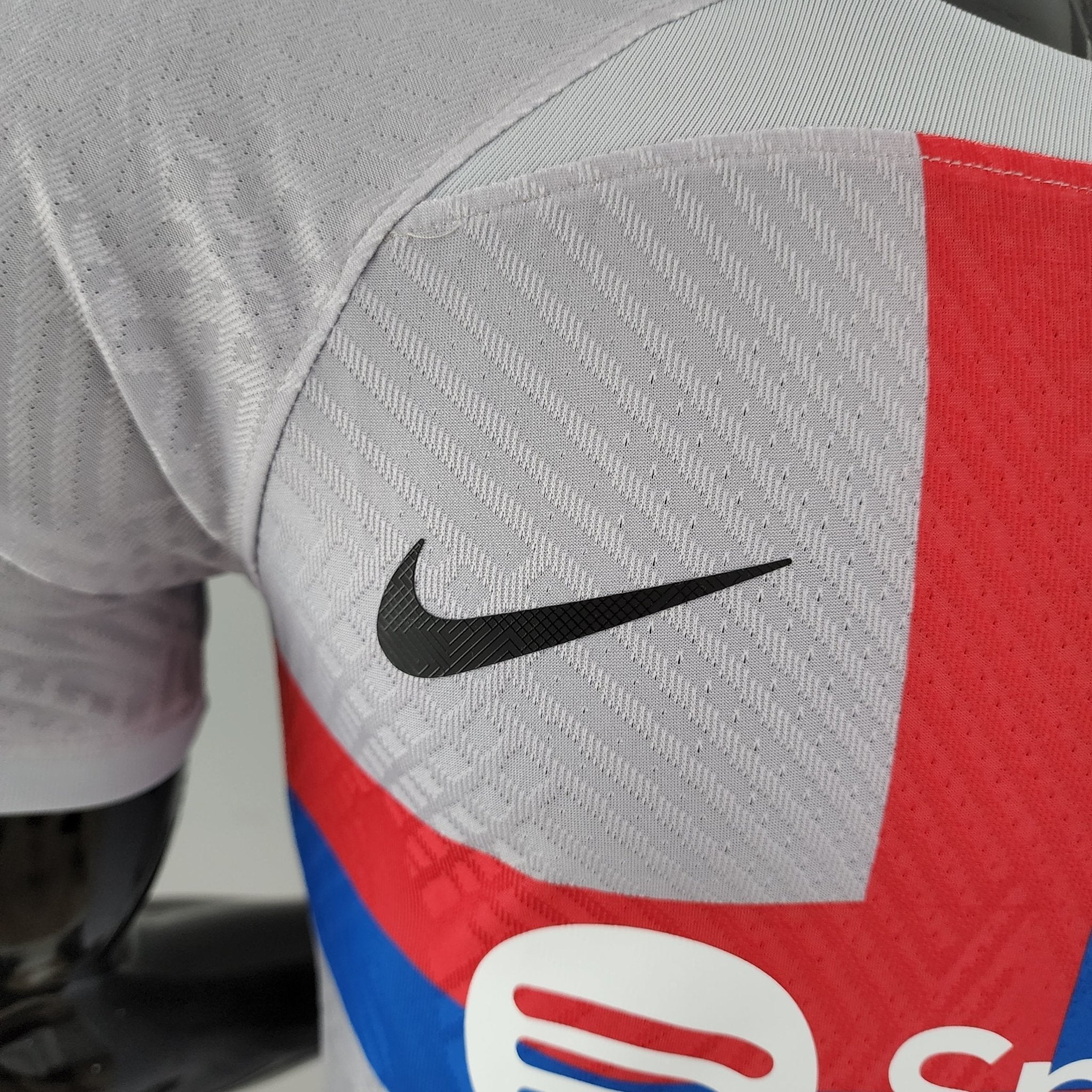 barcelona-third-player-version-jersey-202223-838389 | AE JERSEY Close-up of light gray textured fabric with a diagonal weave and a black Nike swoosh on a red panel.