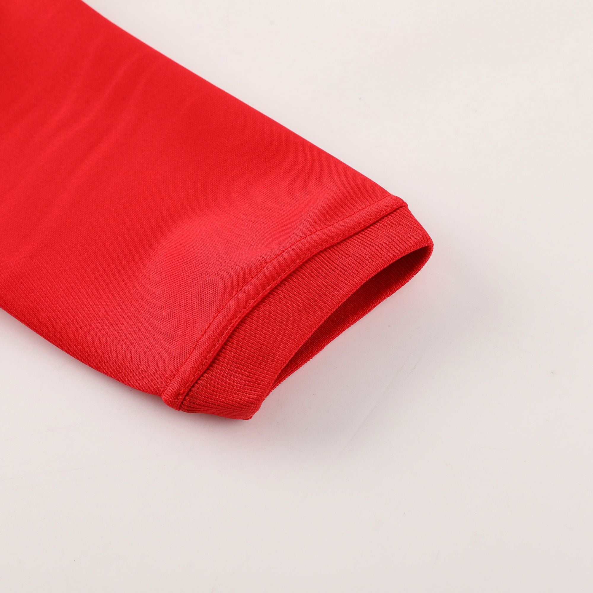 be4a9956 | AE JERSEY Close-up of red fabric with a folded edge and visible stitching against a pale background.