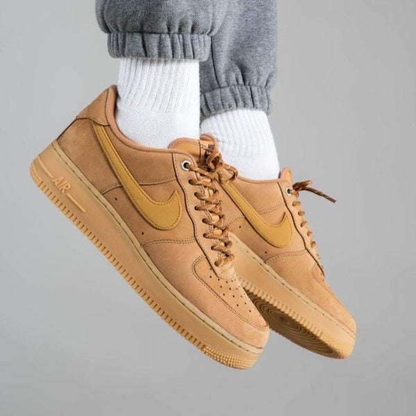 bfee7087-d553-4027-b35c-e60c6add18f0 | AE JERSEY Tan Nike Air Force 1 sneakers with white crew socks and gray joggers, shown midair.
