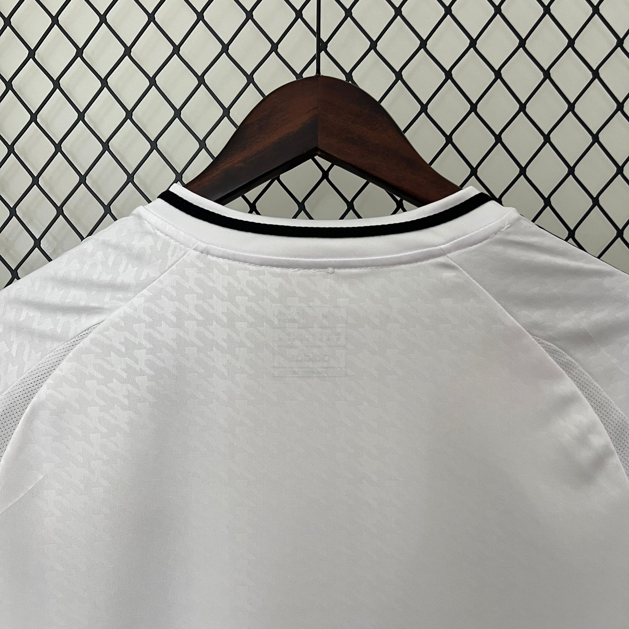 c03b80f6 | AE JERSEY Close-up of a white shirt on a wooden hanger against a chain-link fence backdrop