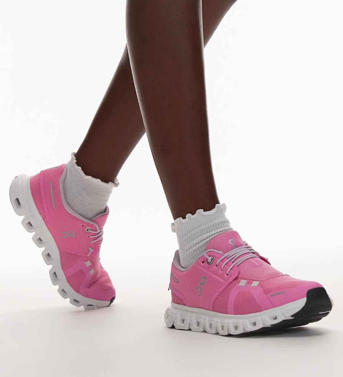 c0994191-972e-492b-afa4-48e978012337 | AE JERSEY Bright pink On running shoes with white chunky soles and white socks on dark legs against a white background.