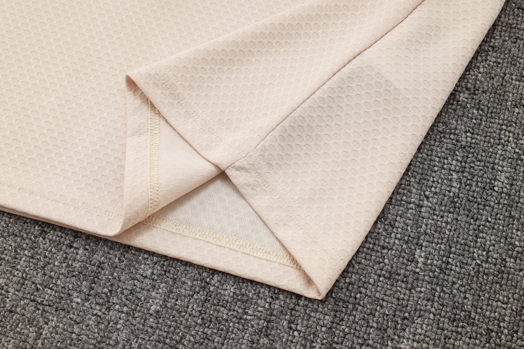 c0a4a0da | AE JERSEY Beige folded towels with a waffle texture laid over a gray carpet.
