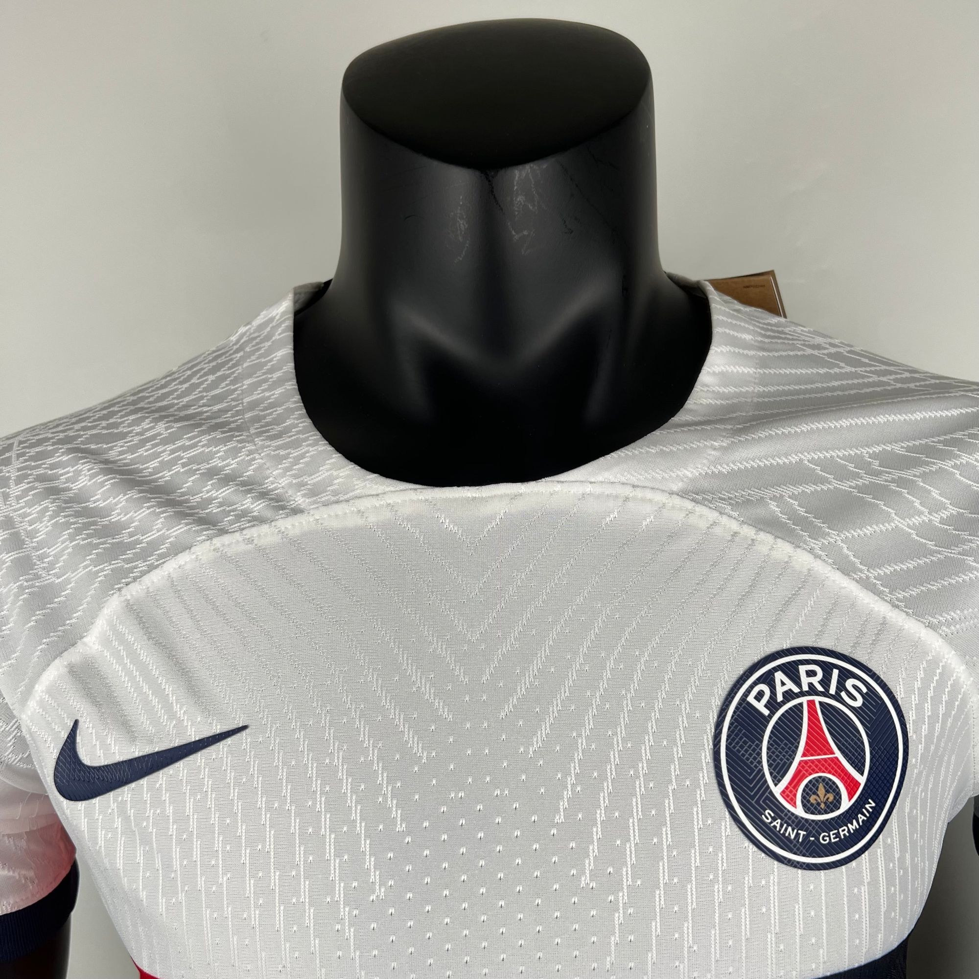 c2ccdbb7_209c24ce-c897-42e6-ba7a-7a6d3ccbc47f | AE JERSEY Gray Paris Saint-Germain soccer jersey on a black mannequin displaying the Nike swoosh and PSG crest.