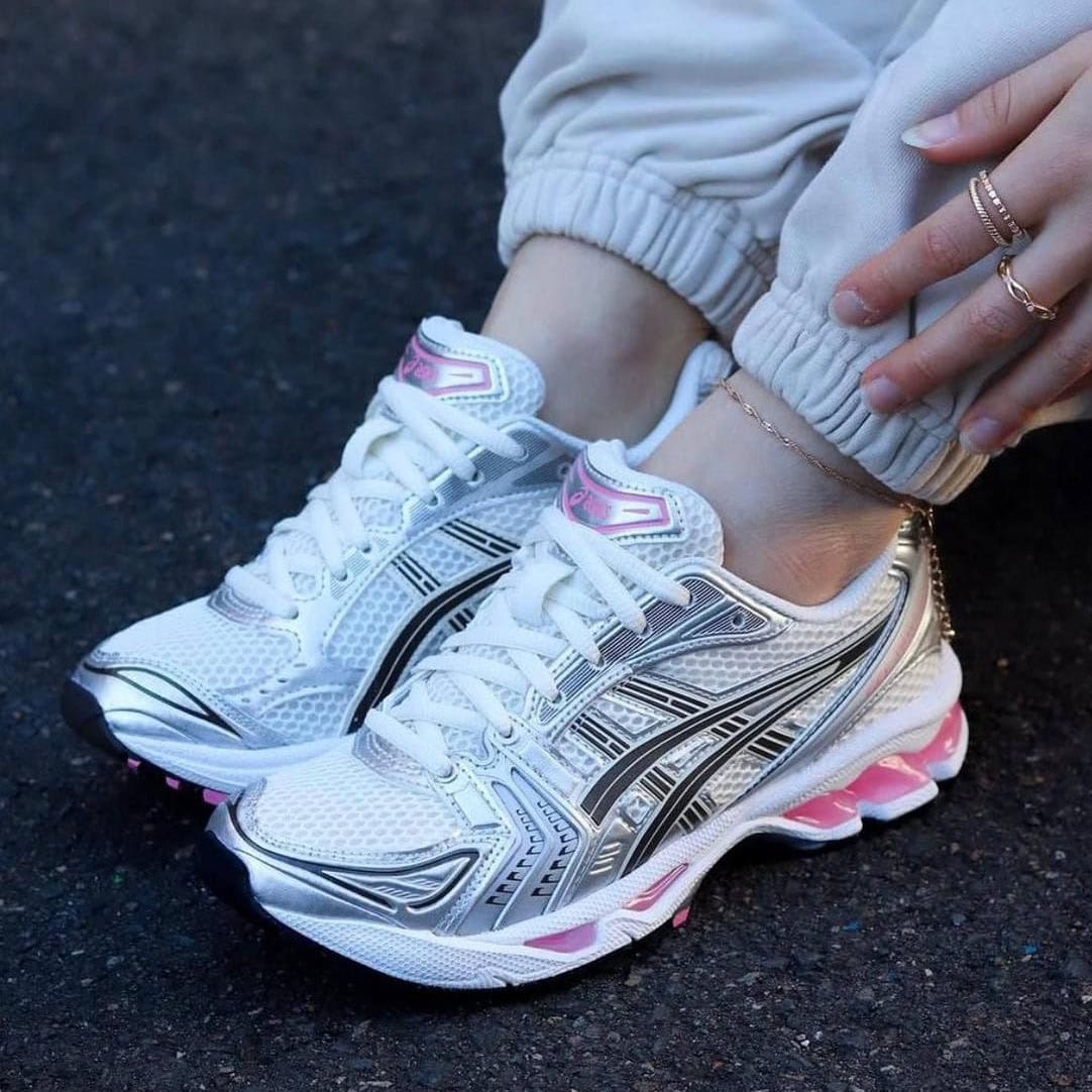 c4668af3-5737-470a-929c-325e461e6dad | AE JERSEY Close-up of white athletic running shoes with pink accents worn with light gray joggers, on dark pavement.