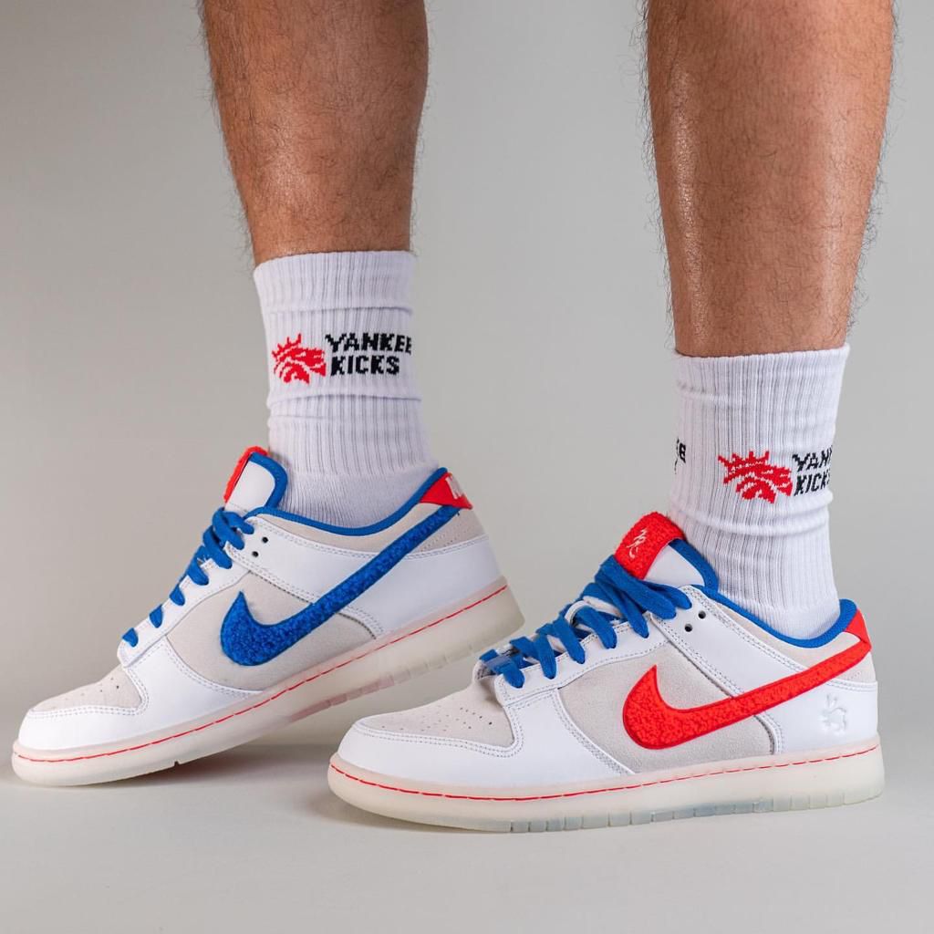 c4e02dd5-c4f8-4a5e-a593-ba24b4b4db65 | AE JERSEY Pair of white sneakers with blue and red accents, worn with white Yankees-themed socks reading 'YANKEE KICKS'.