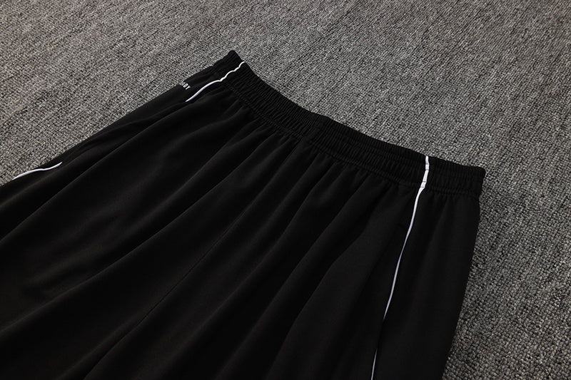 c8feac1e | AE JERSEY Black athletic pants with elastic waistband and white piping, laid on a gray carpeted surface.