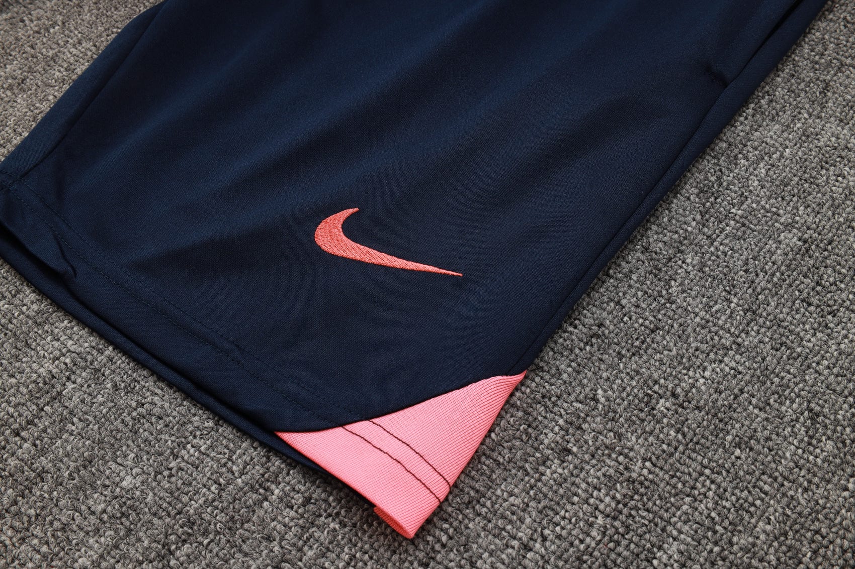 ca5c12a7 | AE JERSEY Close-up of navy athletic pants with a pink embroidered Nike swoosh and pink hem resting on gray carpet.