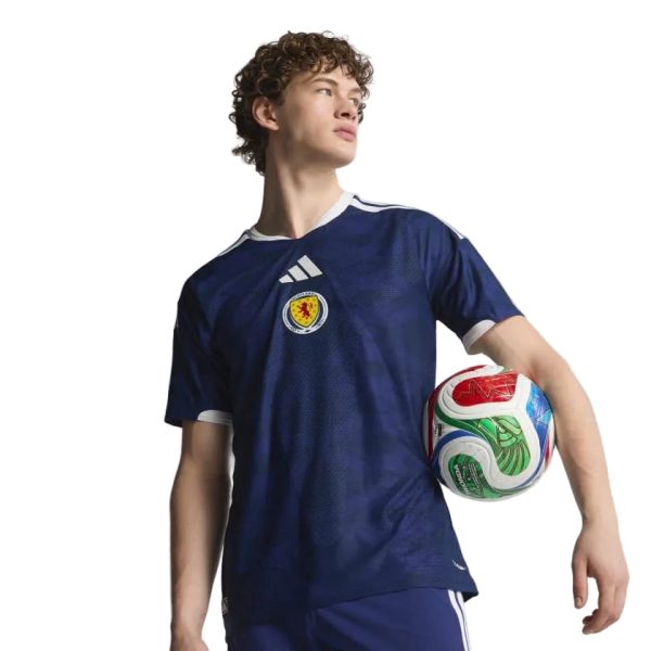 cc927540-7a28-430d-854e-43562c141e2b | AE JERSEY Young man in a navy soccer jersey holds a colorful soccer ball under one arm, looking off to the side against a white background.