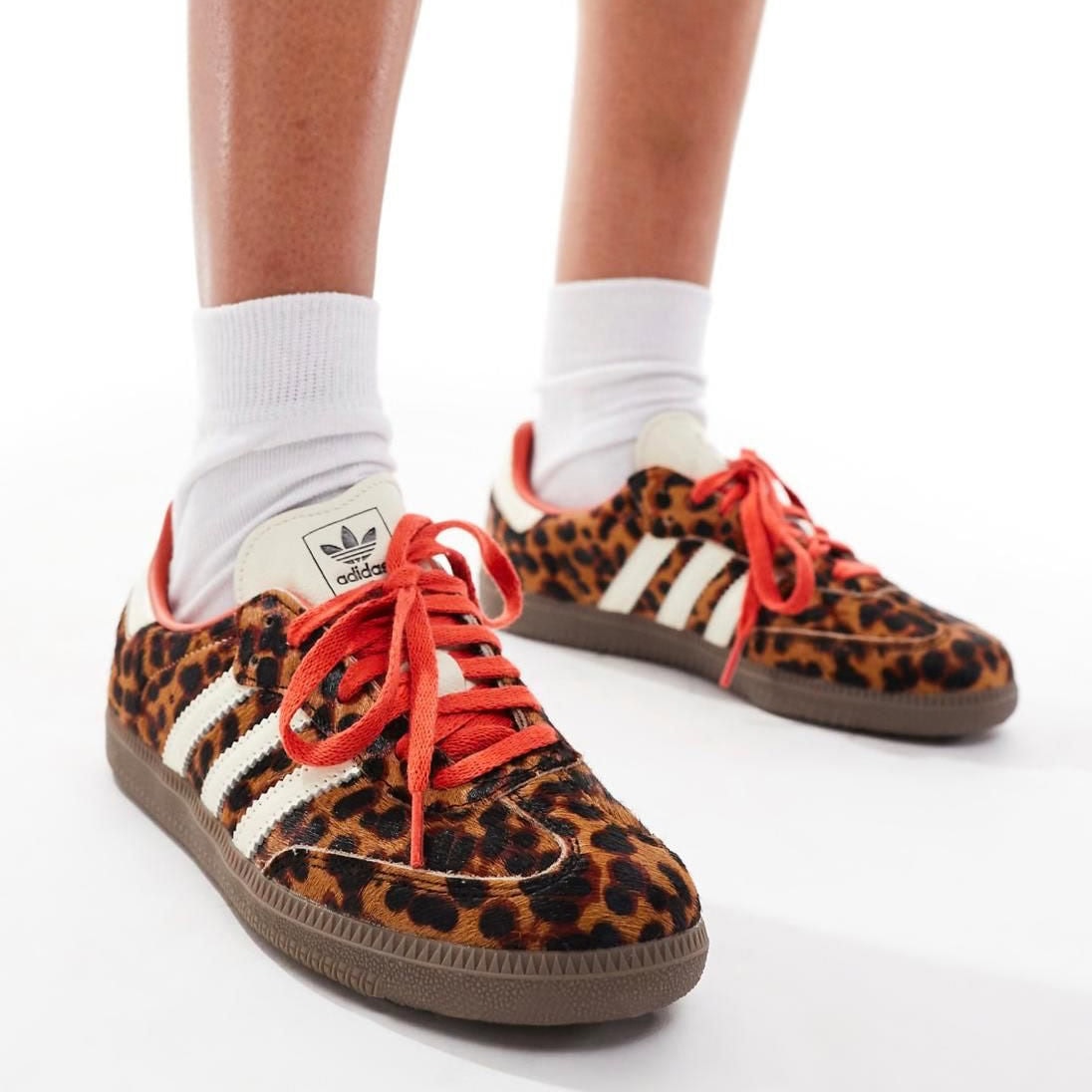 ccb9fd85-cd3d-4d25-a9ae-2b8b6f0291ca | AE JERSEY Feet wearing leopard-print Adidas sneakers with white stripes and red laces, paired with white socks.