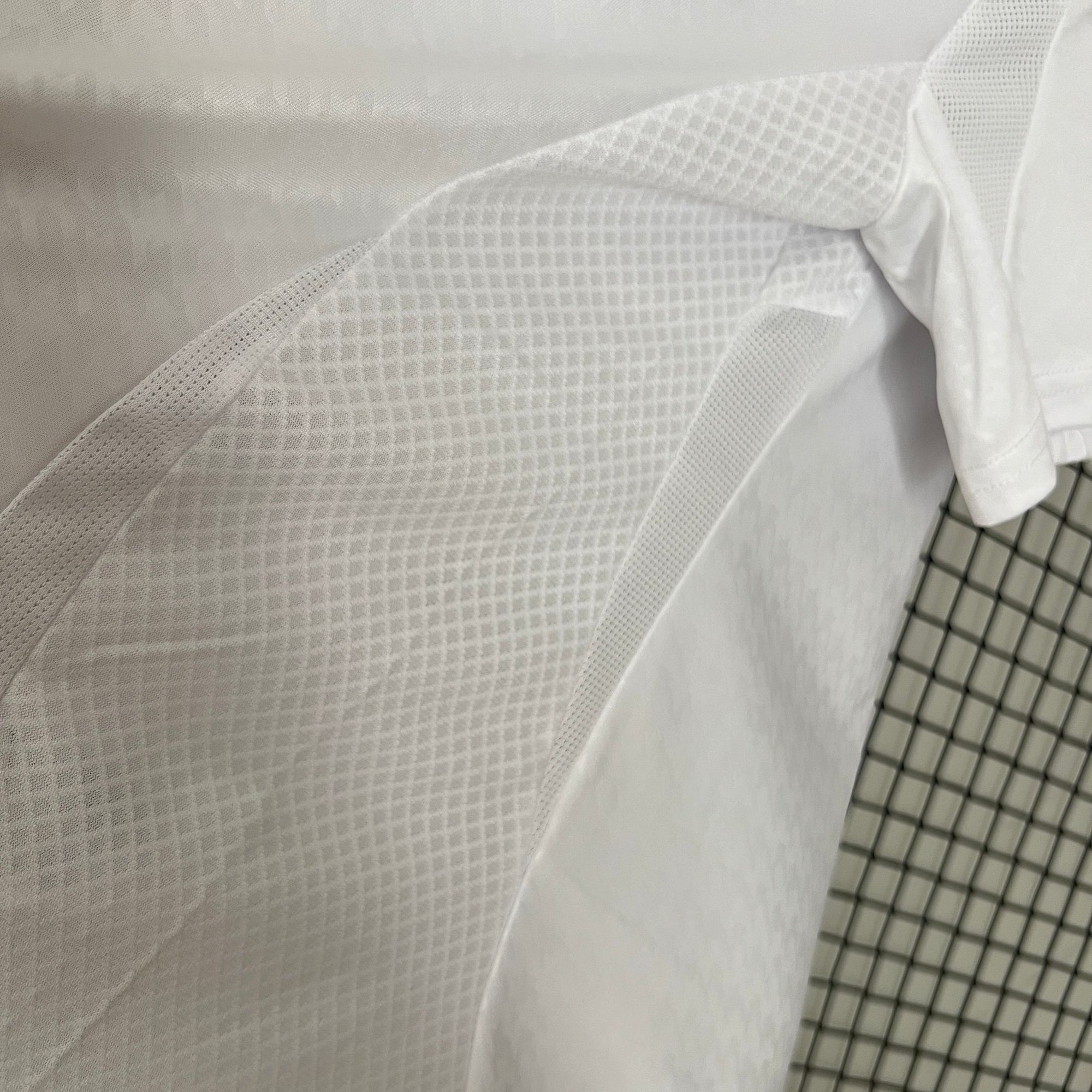 cd2e0040 | AE JERSEY Close-up of layered white fabrics with varying textures and a rolled sleeve on the right.