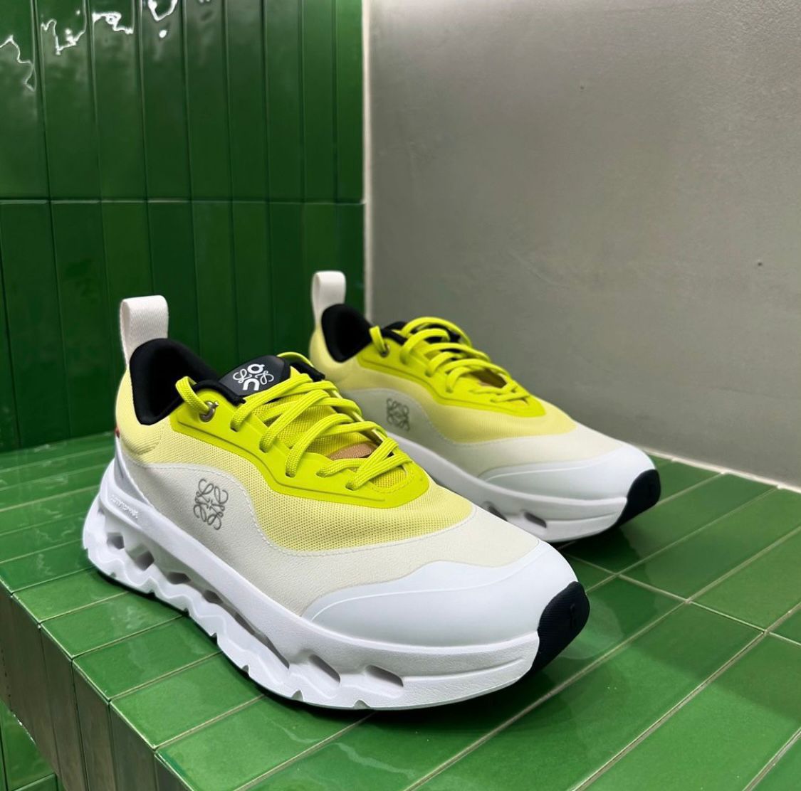 cdf0424b-82fa-4b7e-94bb-246559a69368 | AE JERSEY Pair of bright yellow and white chunky sneakers with thick white sole on a green tiled display shelf, side logo visible.