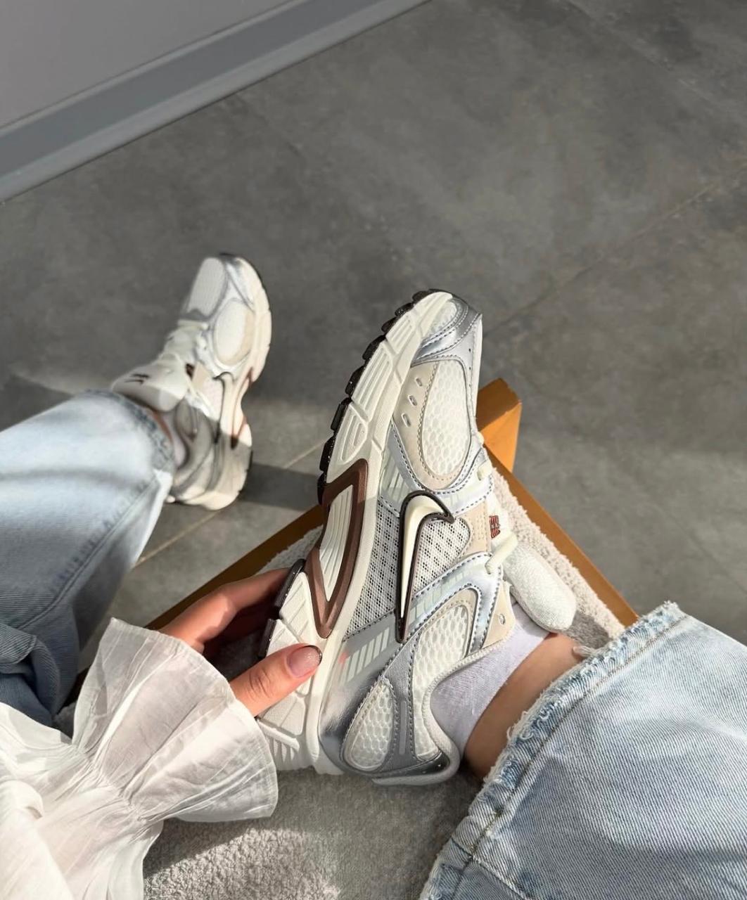 d2a6688e-e383-4c1a-9d8c-7aecb51b9f5d | AE JERSEY Person wearing light-wash jeans holds a chunky white and gray sneaker, showing the side and sole from above.