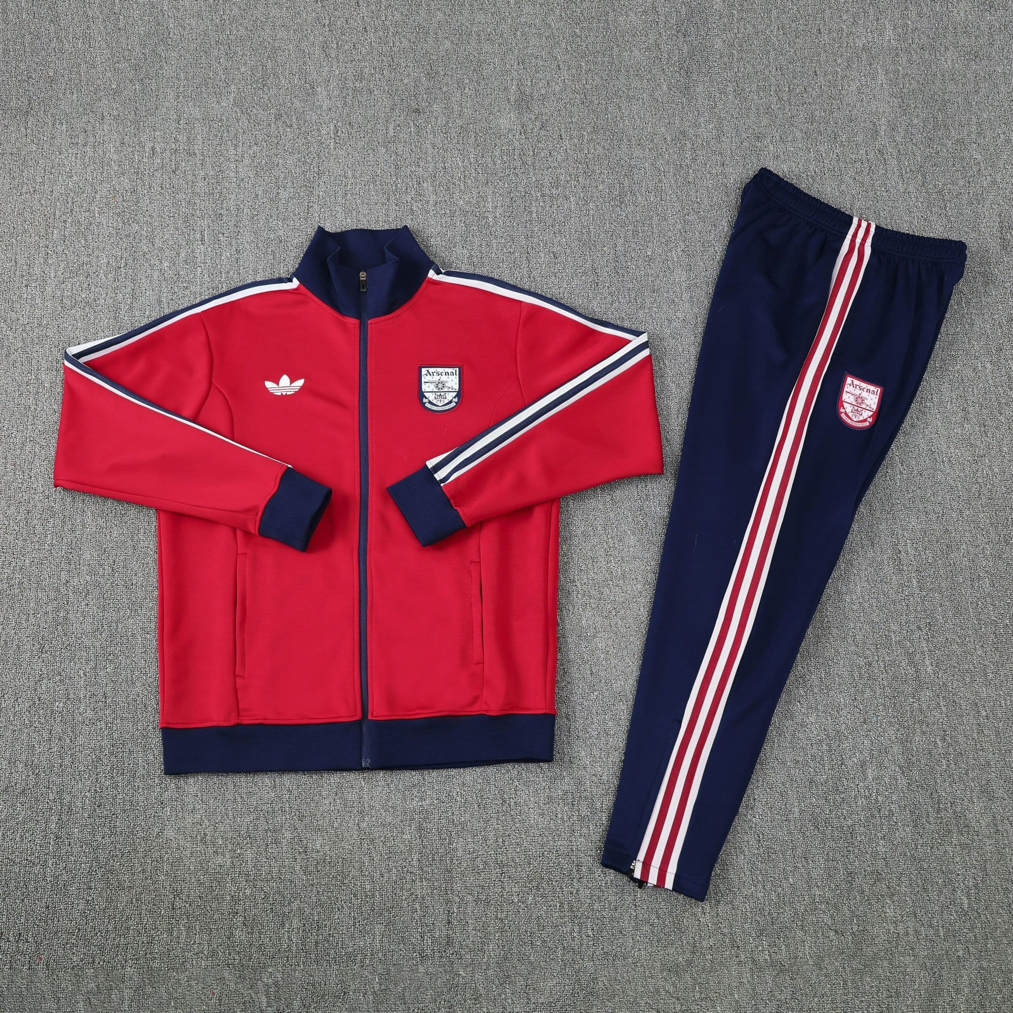 d5179b73 | AE JERSEY Red Arsenal track jacket with navy cuffs and white stripes laid beside matching navy track pants on a gray carpet, outfit ready to wear.