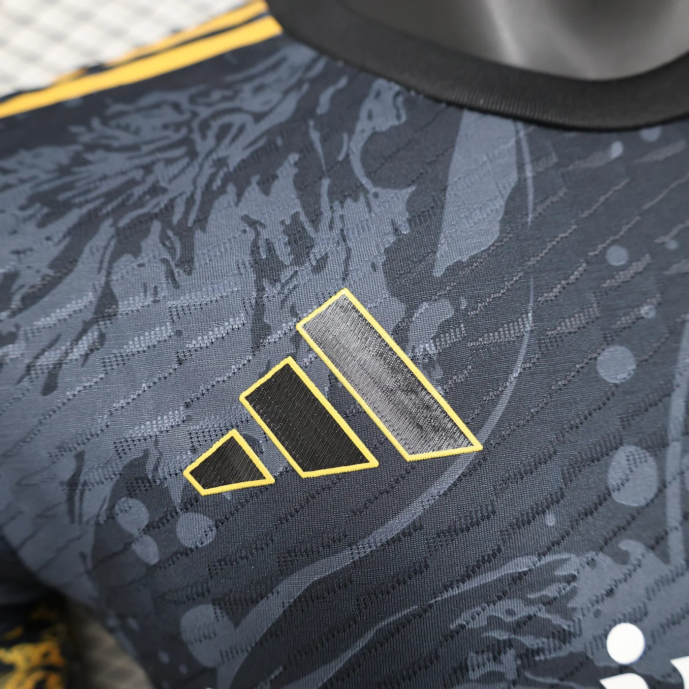 d566dc95 | AE JERSEY Close-up of a dark camo-pattern sports jersey with a yellow-outlined three-bar Adidas-style logo on the chest area.