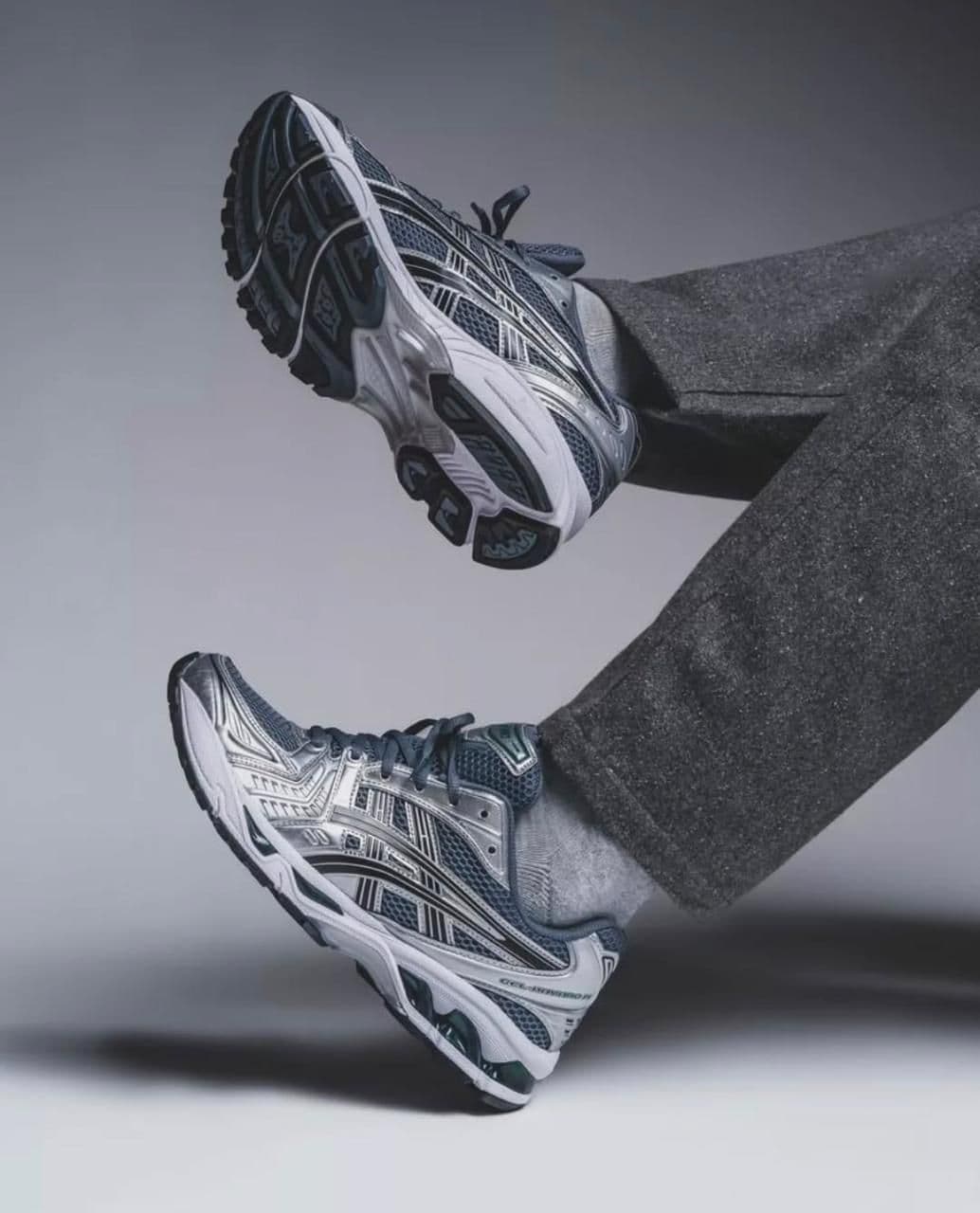 db87a82a-4d69-4e23-a183-eabb92b149a9 | AE JERSEY Two gray and white running shoes suspended mid-air as if kicked up in a jump against a neutral background.