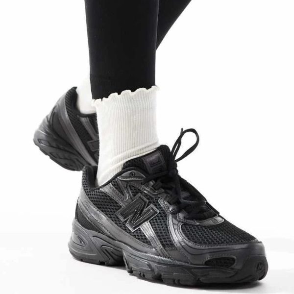 Black athletic sneaker on a person wearing white ribbed socks, with one foot raised for the pose.