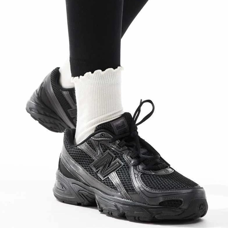 dc706dda-7e21-4774-90b1-01170701000c | AE JERSEY Black athletic sneaker on a person wearing white ribbed socks, with one foot raised for the pose.