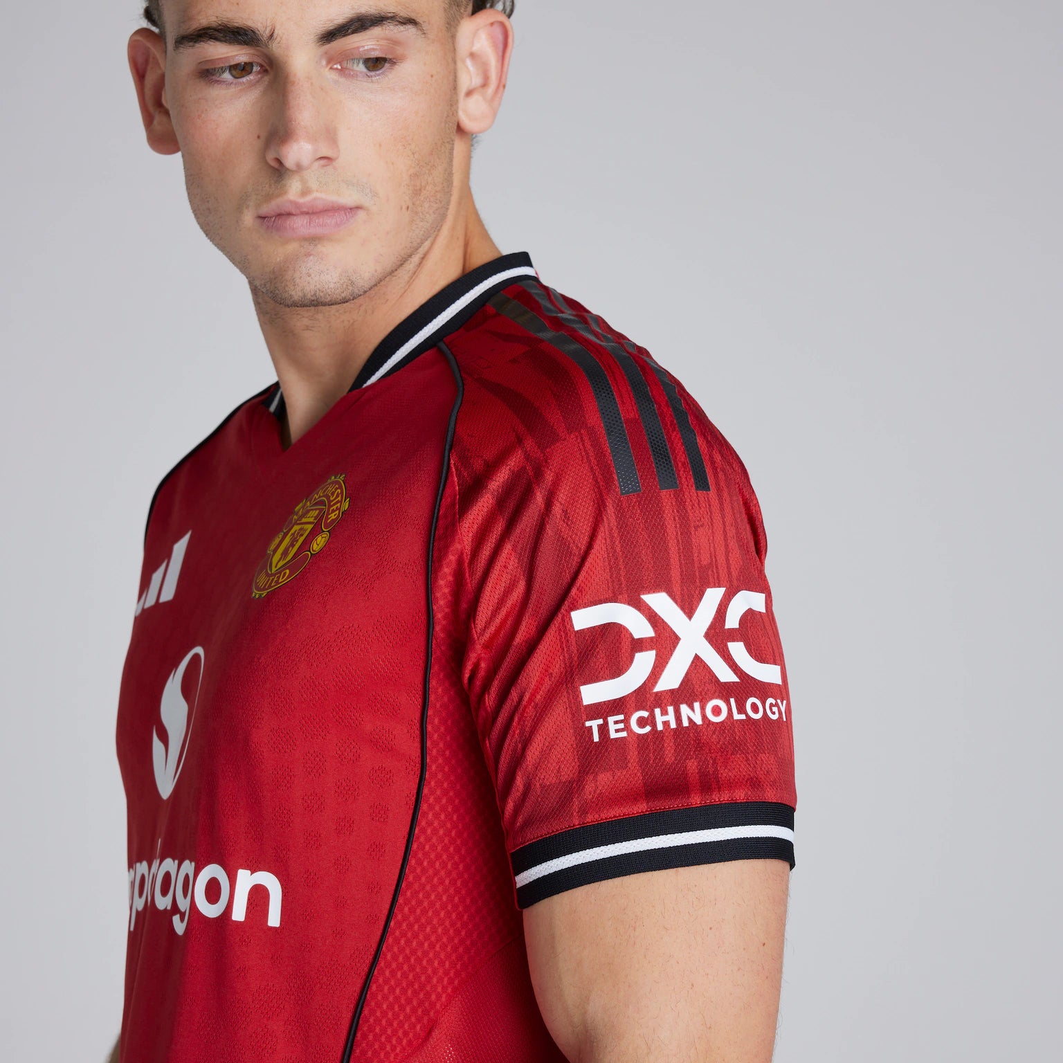 ddce9c8d6c1c0f410823c8943a7d9a9c | AE JERSEY Close-up of a man wearing a red Manchester United jersey, showing the team crest on the chest and sponsor text on the sleeve (side profile).
