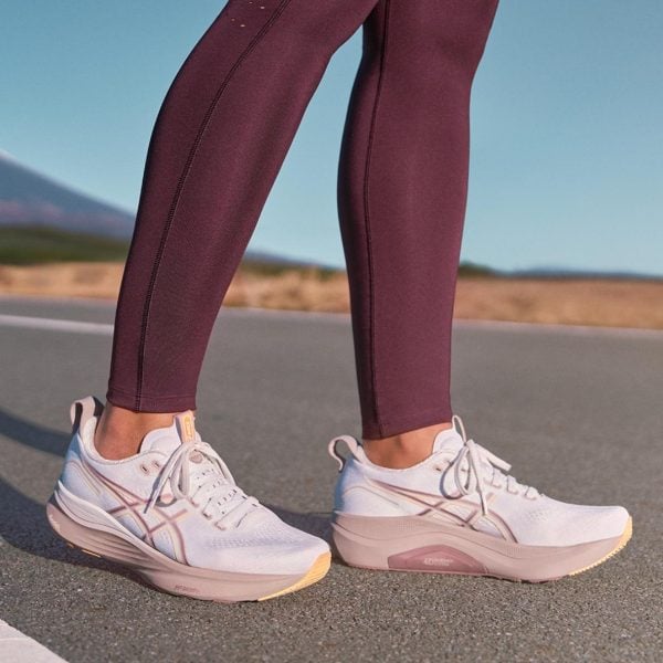 Close-up of a person wearing burgundy leggings and white pink-accent athletic shoes standing on a paved road outdoors.
