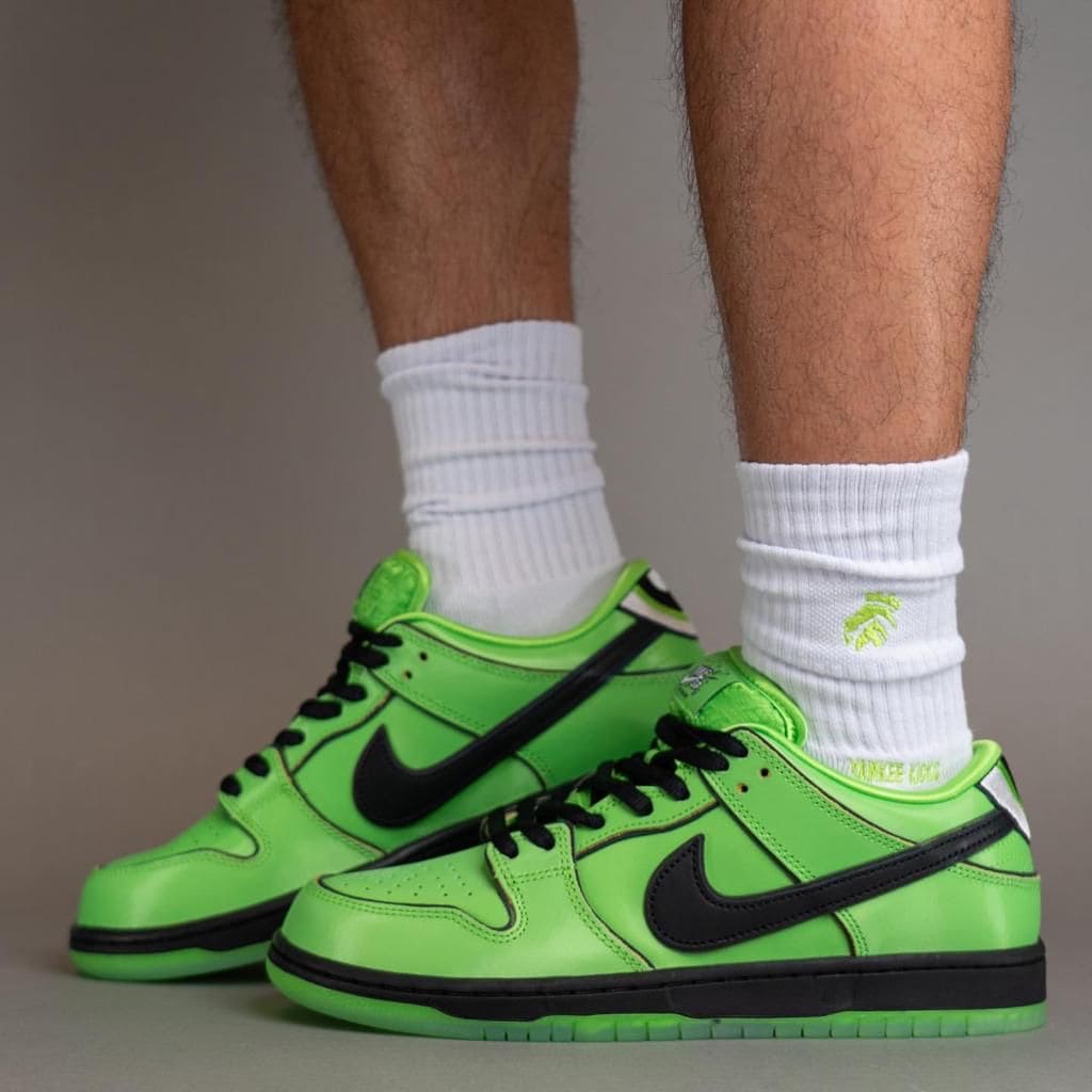 e036fb1d-435b-4084-bded-ca38e8cab33f | AE JERSEY Neon green Nike sneakers with black swooshes on white socks, worn by a person standing on a neutral surface.