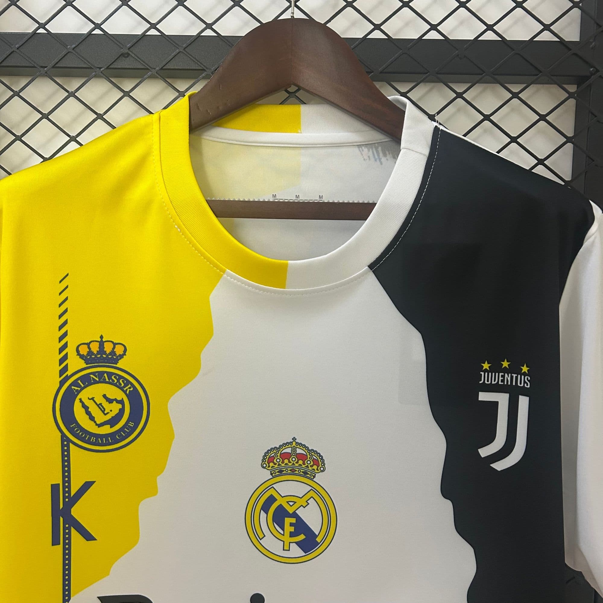 e655999a | AE JERSEY Close-up of hanging football jerseys showing club crests (Al Nassr, Real Madrid, and Juventus) on yellow, white, and dark fabrics.