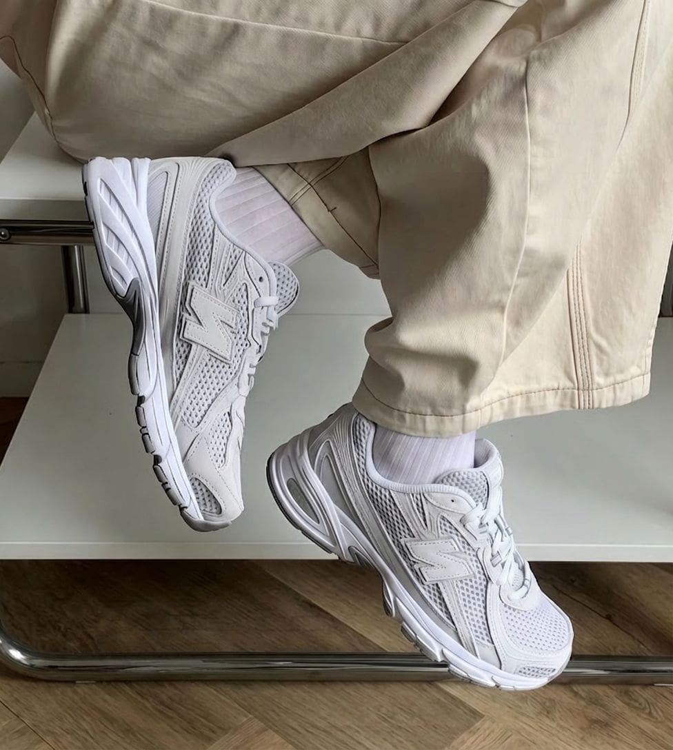 e93ee9c0-c036-4922-8042-c9419a55979e | AE JERSEY White New Balance sneakers on a person wearing beige pants, legs crossed while sitting on a chair, close-up shot.