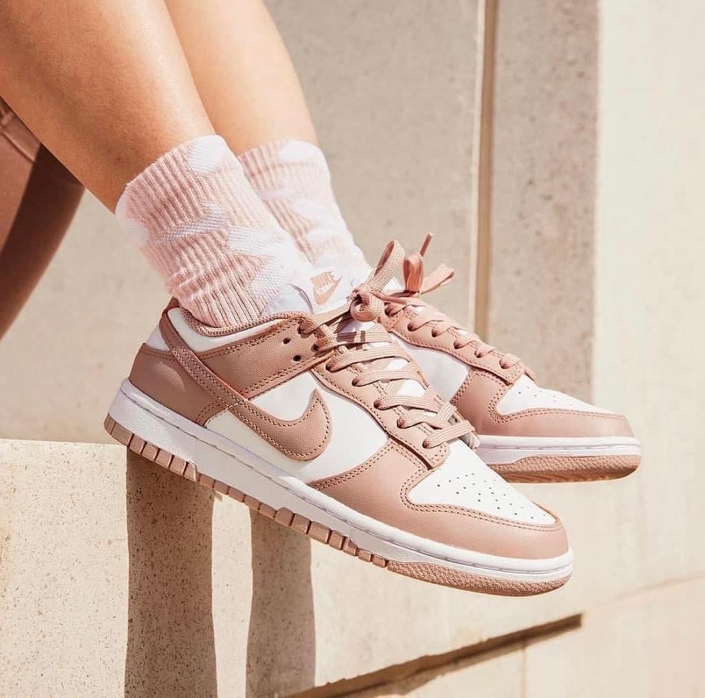 e94c2a50-f6b3-403d-9ded-dcfdeddfaaa3 | AE JERSEY Rose-pink and white sneakers with pink laces, worn with pink patterned socks, perched on a stone ledge.