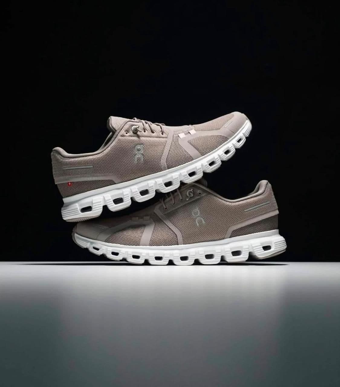ea8d2b2f-d3f4-4b29-b0e5-f51f85ecdca8 | AE JERSEY Pair of beige mesh running shoes with white soles stacked one atop the other against a dark background, showcasing textured upper and cutout sole design.
