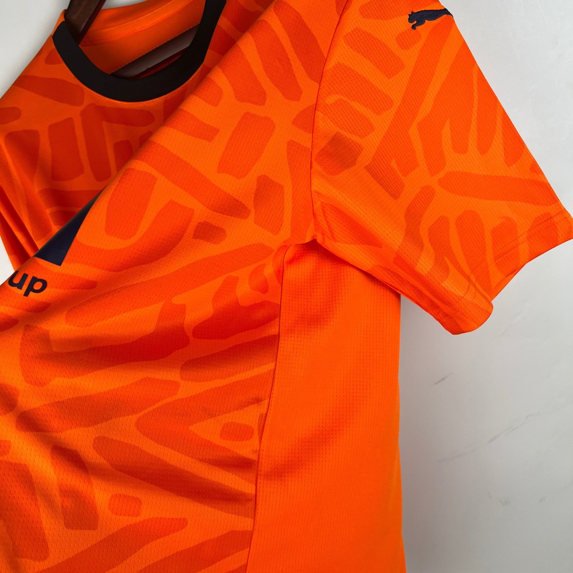 ece78b80_c9064bad-5959-442a-a323-d6152fd13c06 | AE JERSEY Close-up of a bright orange high-visibility jacket with a black Puma logo on the shoulder.