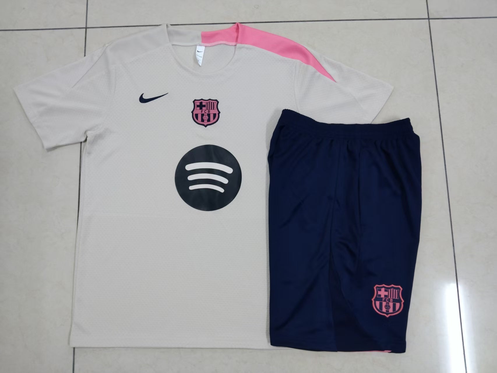 ed1cf881 | AE JERSEY White FC Barcelona soccer jersey with pink shoulder accent, navy Nike swoosh, pink crest, and Spotify logo on the chest, paired with navy shorts on a tiled floor