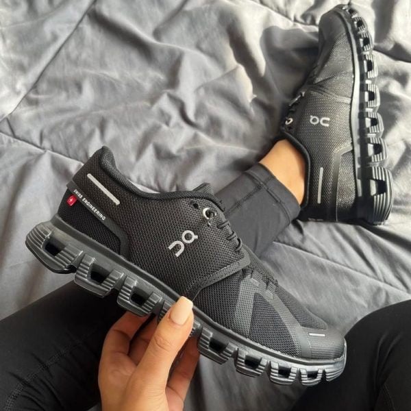 Black On running shoe with the brand's unique hollow segmented midsole, shown from the side while resting on a bed surface.