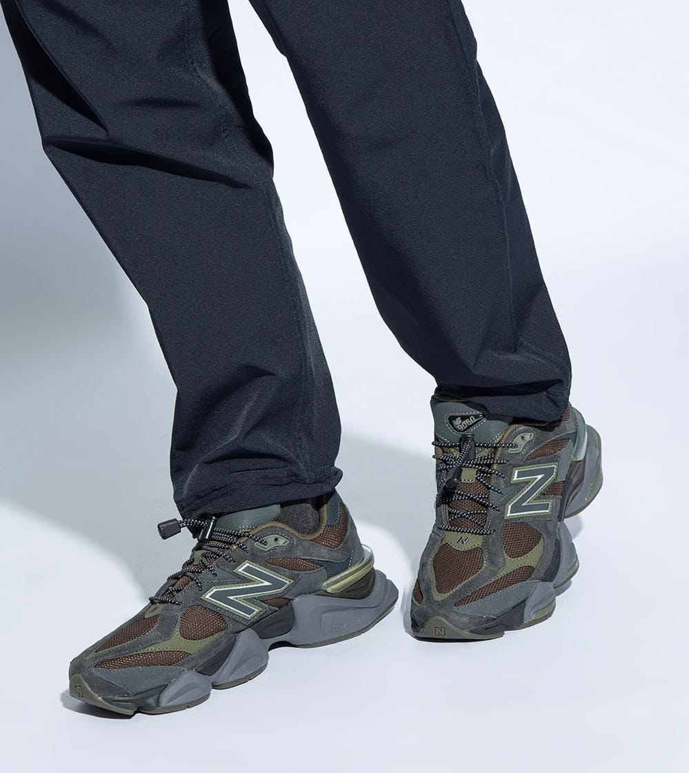 eee1f7ab-736d-4b8d-aadc-e809720e941b | AE JERSEY Person wearing dark pants and gray-green hiking sneakers with a prominent 'N' logo.