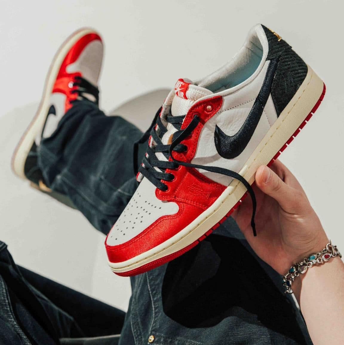 f00ec8b1-59f1-478b-a347-a9e69fe598ef | AE JERSEY Close-up of a hand holding a red, white, and black Nike Air Jordan 1 sneaker against a light background