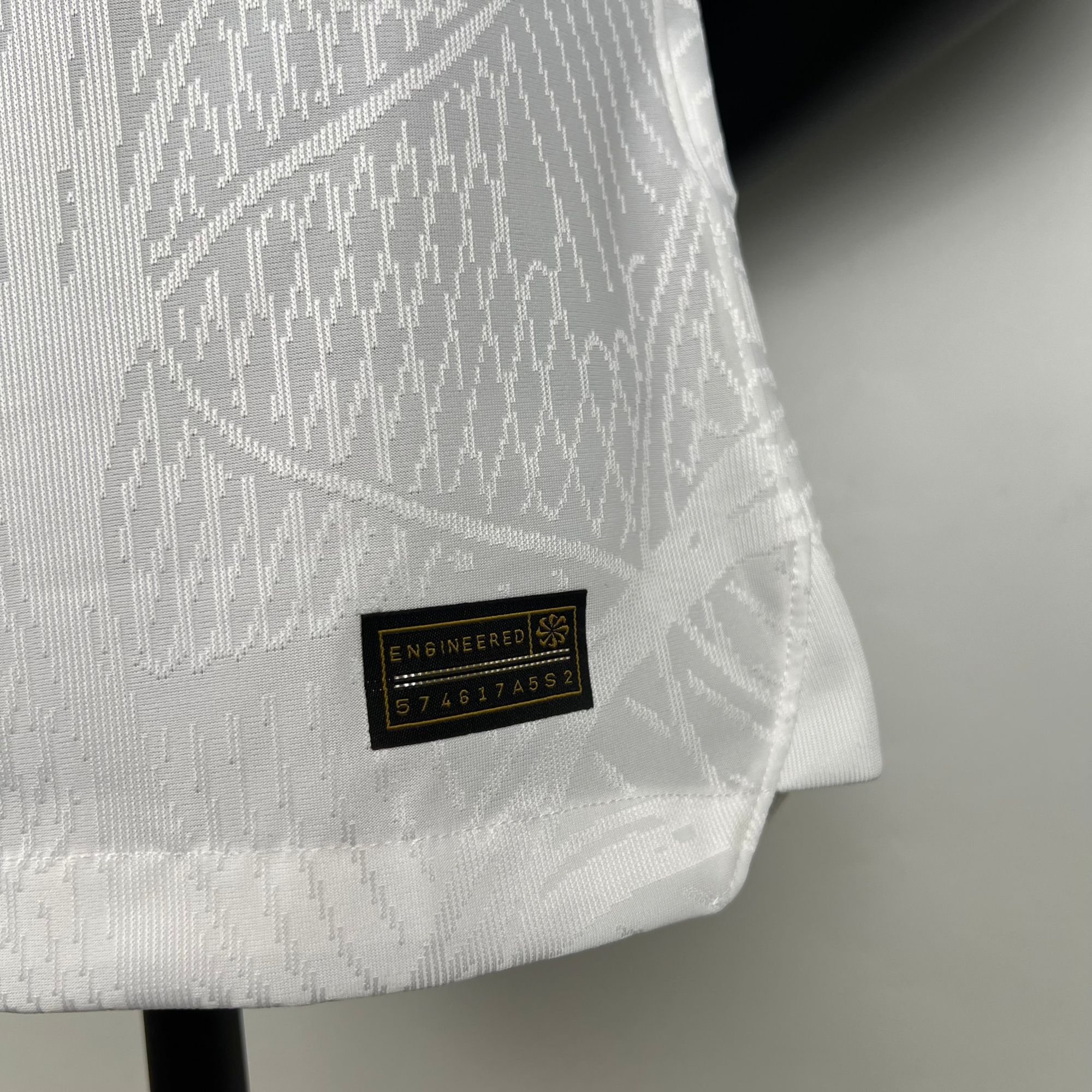 f2613008_d3fc2d4c-104f-47a2-bcb8-32c967aa1ab9 | AE JERSEY Close-up of white patterned fabric with a small black label that reads ENGINEERED.