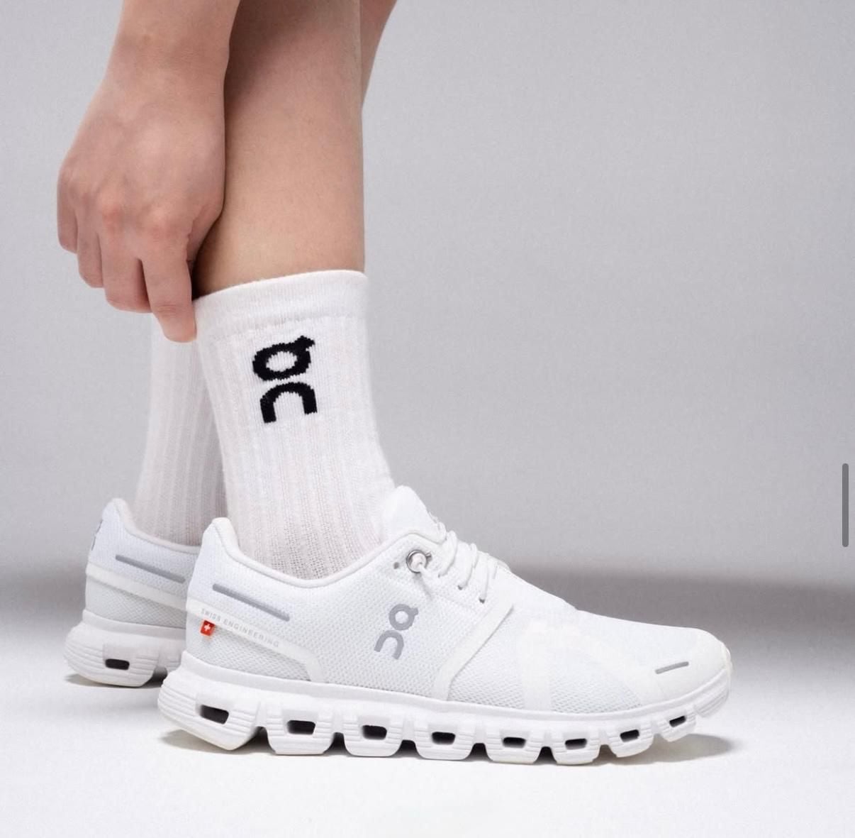 f2eb2dad-8d01-4ad7-9768-771b7c4042f9 | AE JERSEY Close-up of white On running shoes worn with white socks on a light gray surface, side view.