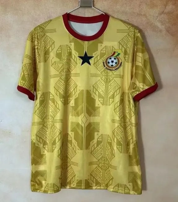 f7a0dea9-b49f-4c3b-98c7-38af384b76fd | AE JERSEY Yellow soccer jersey with red collar and sleeve cuffs, a black star centered on the chest, and a crest with a football on the left. Patterned geometric design all over.