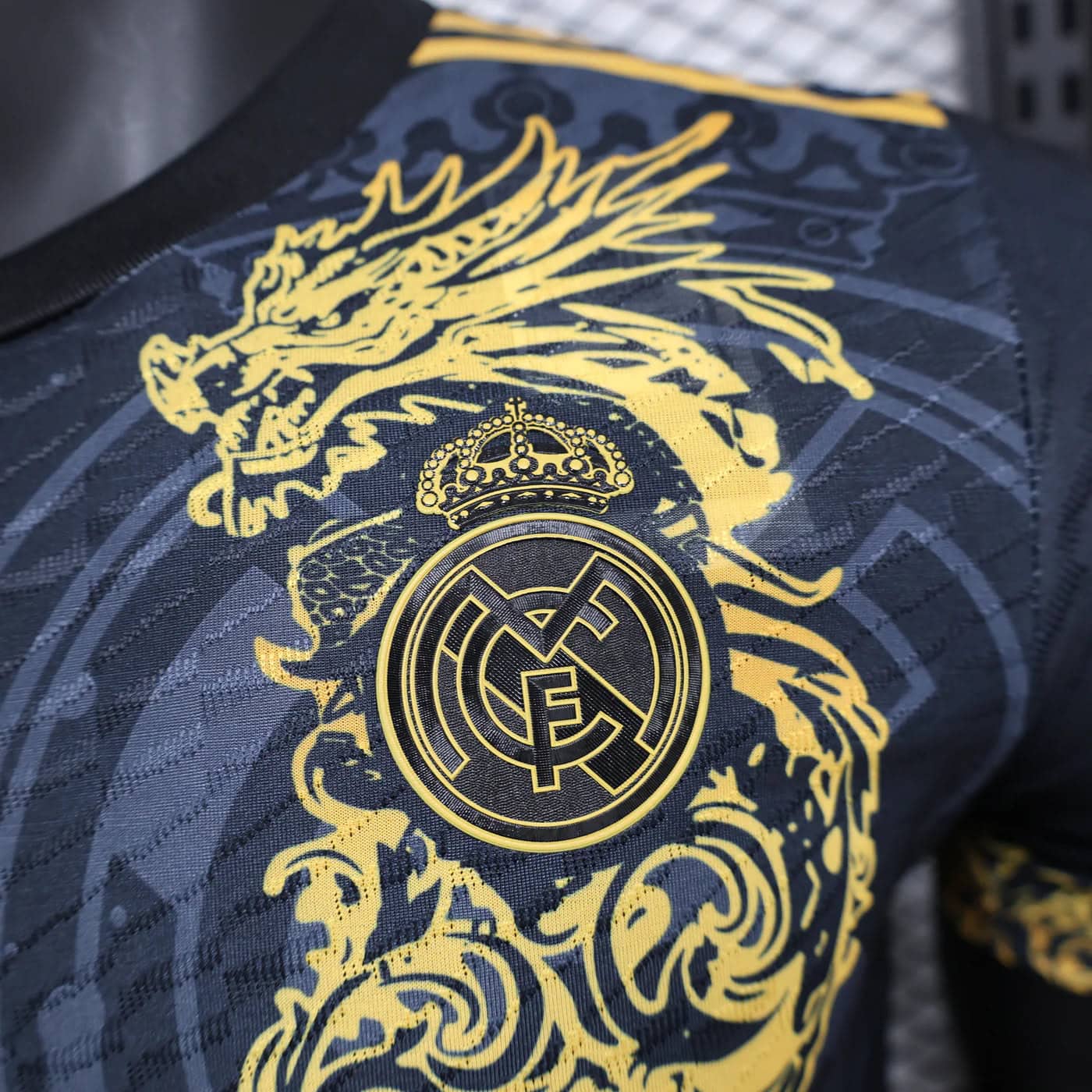 fa266c7e | AE JERSEY Close-up of a gold Real Madrid crest with crown on a dark patterned fabric (jersey).