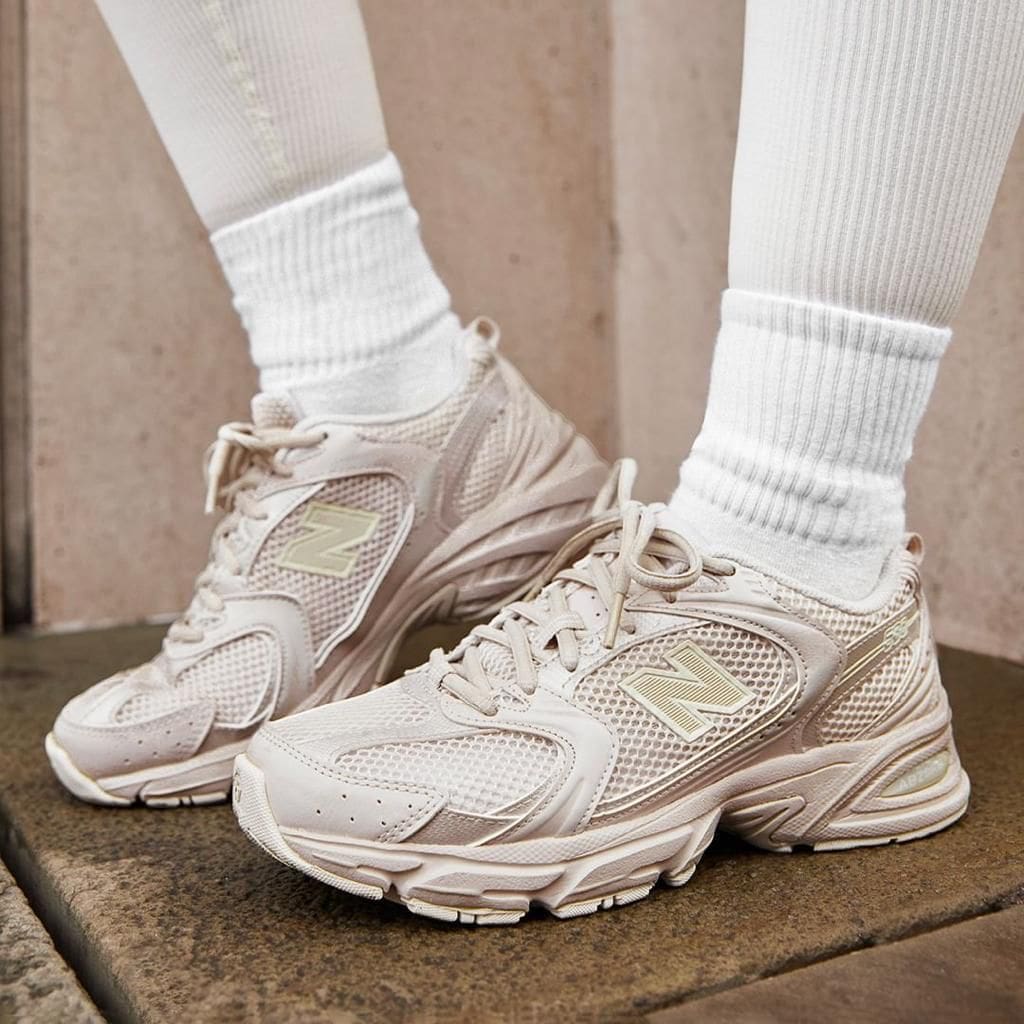 fe1babc8-eada-43be-9cd7-285605f8a892 | AE JERSEY Beige New Balance sneakers with white socks standing on a stone step, highlighting the chunky sole and mesh design.