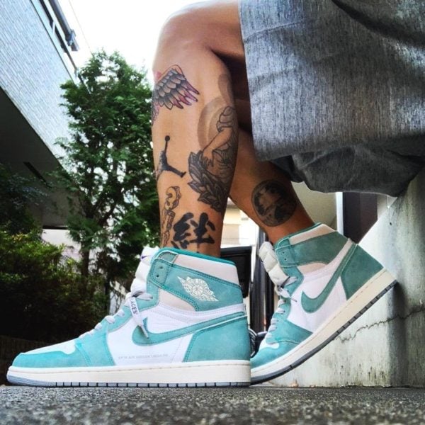 Teal and white high-top sneakers on a tattooed leg, outdoors on a concrete surface.