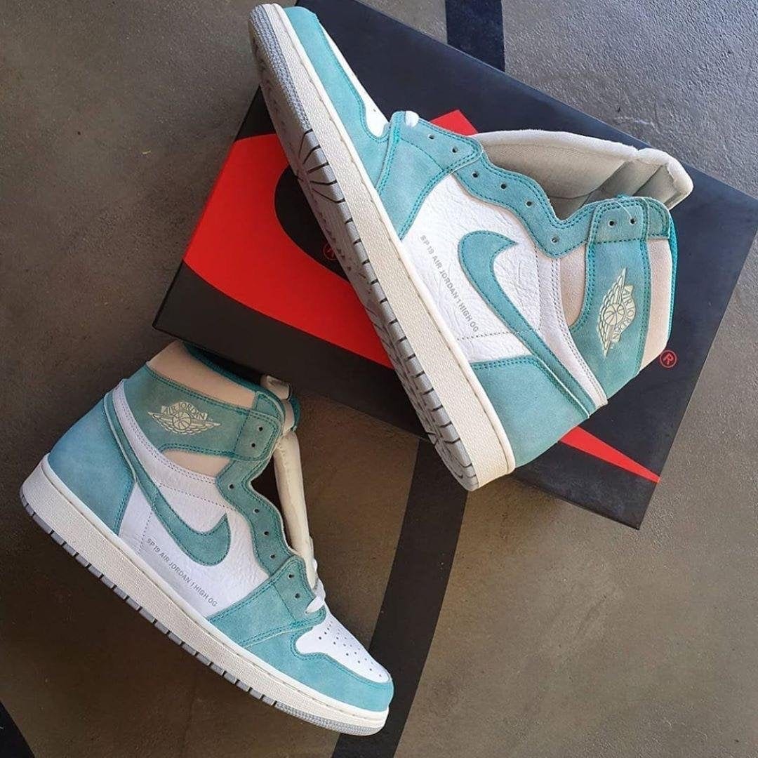 image_dbb3ce55-0f9d-4875-bcea-e987e8621d24 | AE JERSEY Turquoise and white Air Jordan 1 sneakers resting on a black Nike box with a red swoosh.