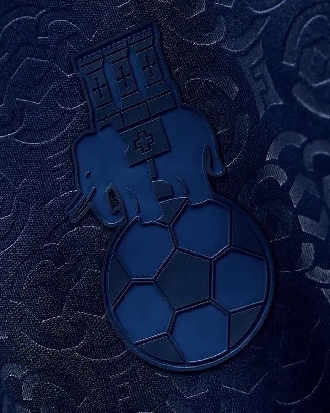 img_8396-1 | AE JERSEY Close-up of a blue insignia shaped like a bomb/grenade with a fortress-like top, placed on dark patterned fabric.