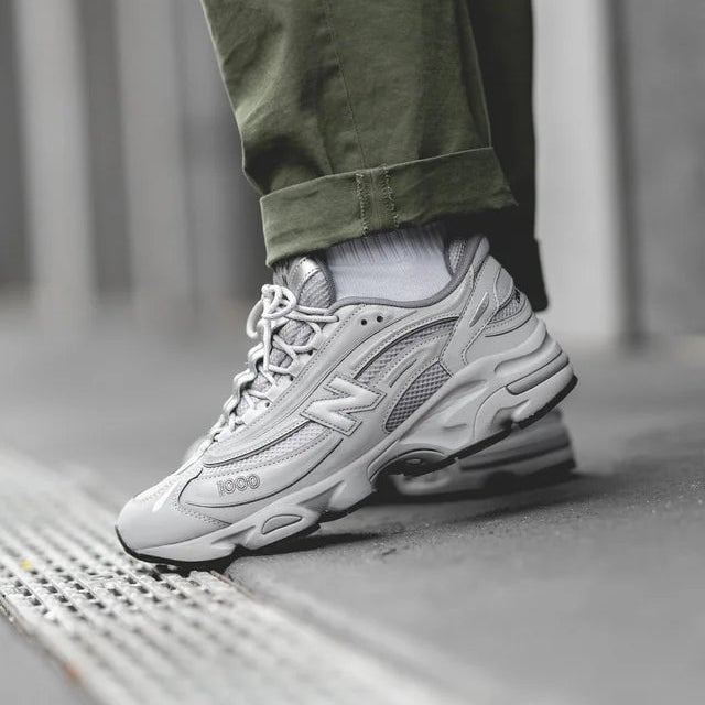 j1pi3avr1oad1 | AE JERSEY Close-up of a gray athletic sneaker stepping on a curb, with olive-green rolled pants visible above the shoe.