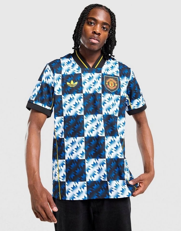 jd_760195_b | AE JERSEY Person wearing a blue and white geometric Manchester United football jersey with Adidas logo and crest, standing against a light gray backdrop.