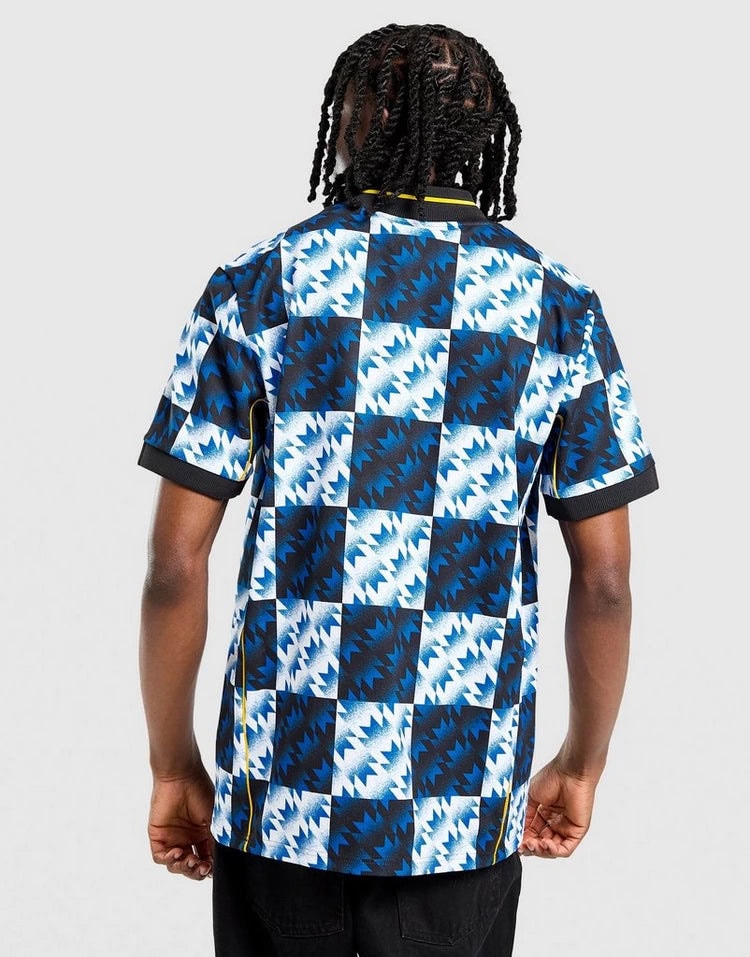 jd_760195_c | AE JERSEY Back view of a person wearing a blue geometric patterned short-sleeve shirt in a checkerboard design, dark jeans visible.