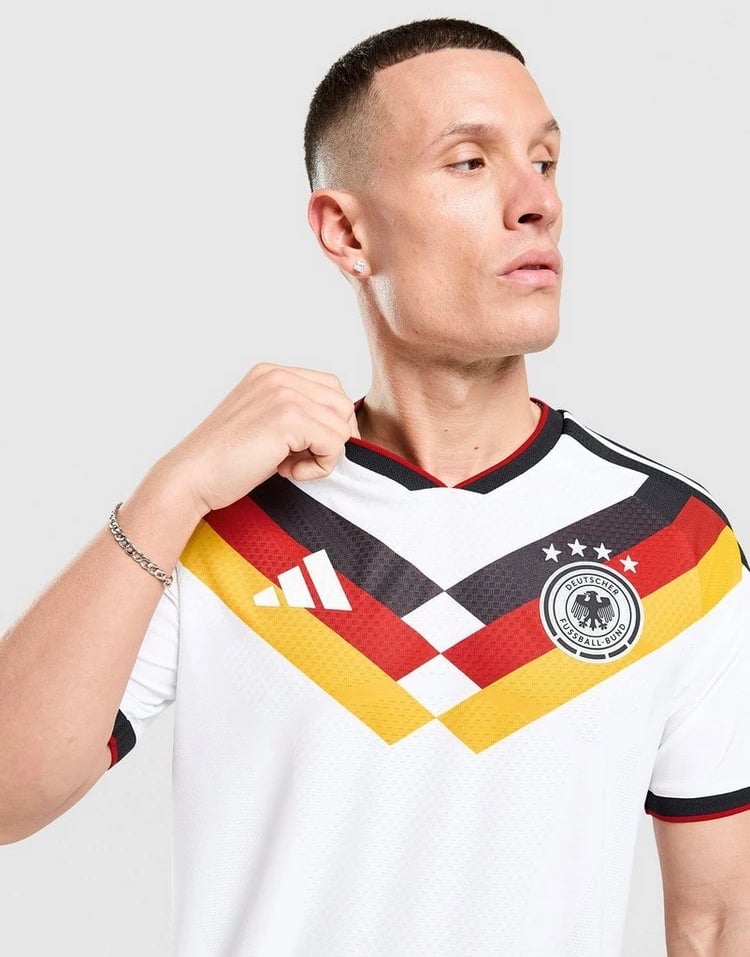 jd_776182_b | AE JERSEY Man wearing a white Germany national football team jersey with black-red-gold chevrons, looking to the right while adjusting the collar.