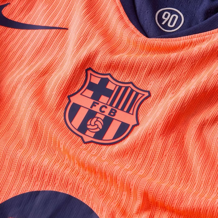 kg | AE JERSEY Close-up of an orange FC Barcelona football jersey with crest and a 90 patch visible on the collar