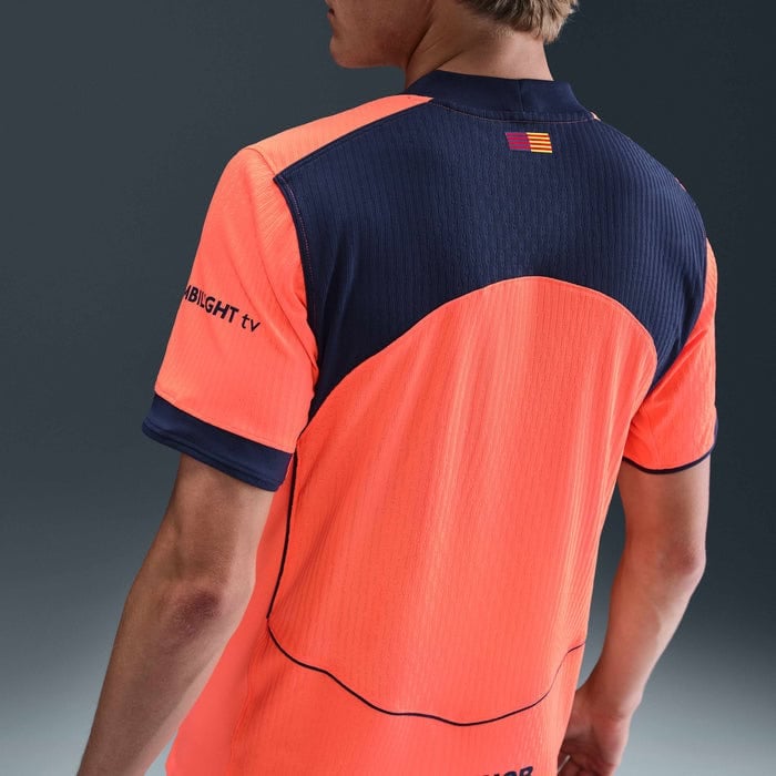 kh | AE JERSEY Back view of a person wearing a neon orange and navy sports jersey with a small striped flag on the upper back and curved seam details.